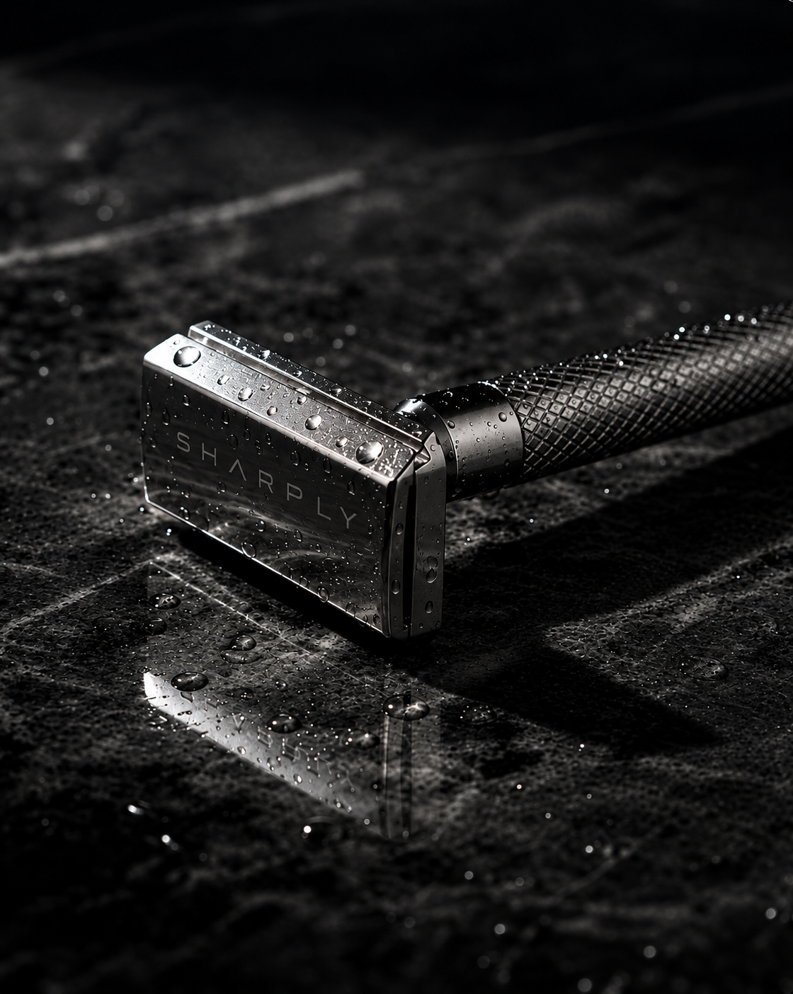 Close view of the Sharply Blade One head on wet stone, water beaded on the polished 316 stainless steel and the engraved SHARPLY wordmark