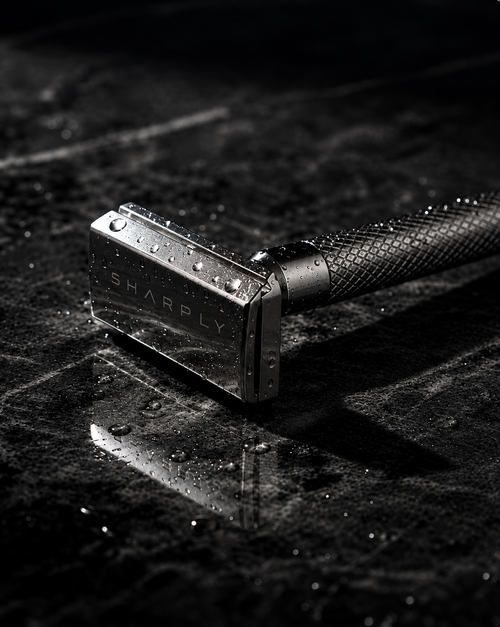 Close view of the Sharply Blade One head on wet stone, water beaded on the polished 316 stainless steel and the engraved SHARPLY wordmark